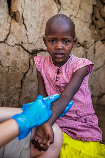 Female doctor is doing an injection to little African girl in small Masai village, Southern Kenya. Maasai tribe inhabiting southern Kenya and northern Tanzania, and they are related to the Samburu.