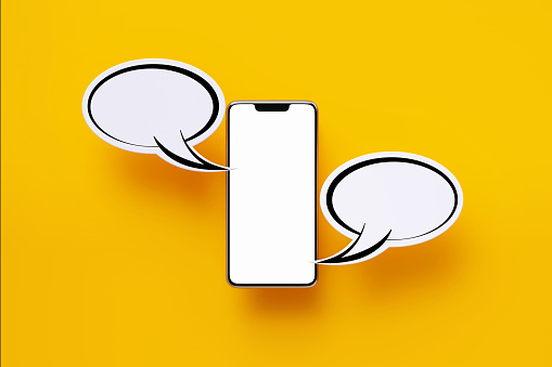 Smart phone and white chat bubbles sitting over yellow background. Horizontal composition with copy space. Online messaging and social media concept.
