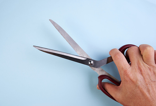 Hand holding scissors isolated on blue background