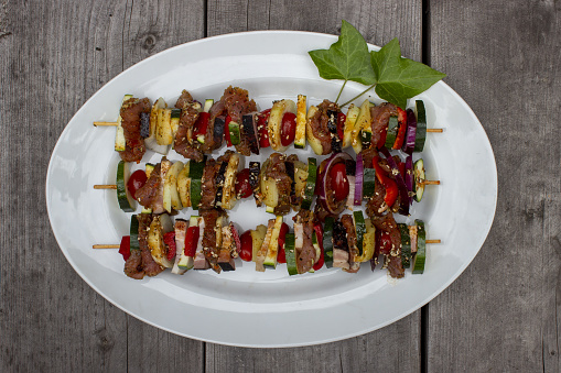 Skewer before grilling composed of bacon onions tomatoes meat pork zucchini peppers on a plate with leaves on a wooden table