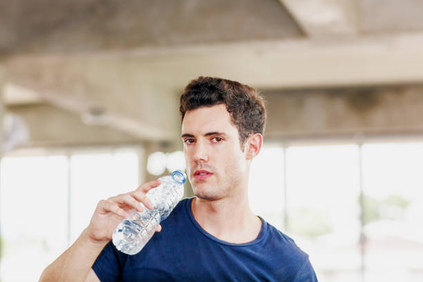 istock handsome man drinking water directly from the bottle after excercise in the modern gym 1257030590