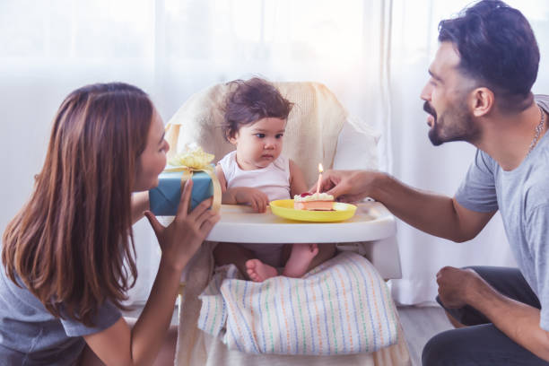 one year old little girl or toddler daughter get celebrate of birthday party at home her father and mother give cake and gift box to their beloved. adorable little girl surprise, look birthday candle - child party group of people little girls imagens e fotografias de stock