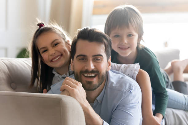 istock Smiling young dad lying on sofa with adorable small children. 1257040919