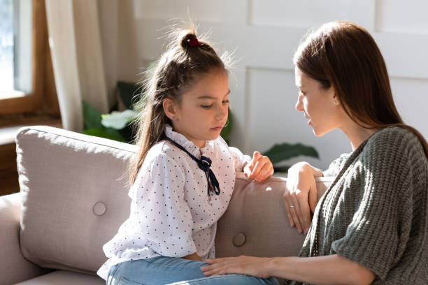 Upset small schoolgirl having trustful conversation with mother. Upset small schoolgirl having trustful conversation with compassionate young mother, sitting together on sofa. Wise mommy comforting soothing little child daughter, overcoming problems at home. parent stock pictures, royalty-free photos & images