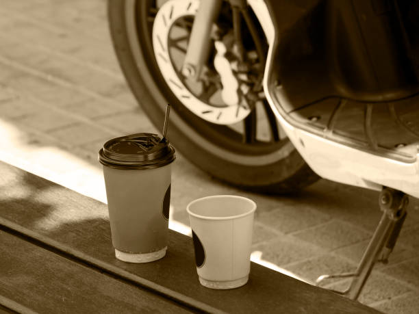 Paper coffee cups on street bench near motorcycle