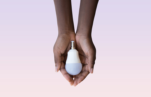 Black woman's hand holding a white light bulb on a pink background