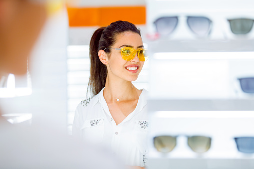 Smiling young woman trying yellow sunglasses on in eyewear shop