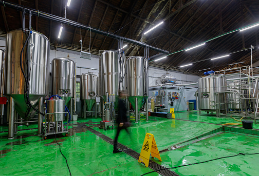 Unrecognizable worker in brewery walking between fermenting tanks in production premises