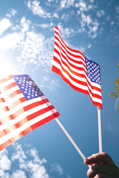 istock Hand holding two american flags on the blue sky with sunlight background, waving flag for United States of America close-up 1257047909