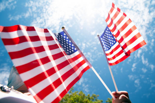 istock Hand holding two american flags on the blue sky with sunlight background, waving flag for United States of America close-up 1257048551