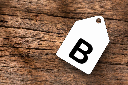 Letter B on white label on wooden background