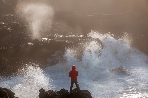 Fearless young female photographer taking pictures while surrounded by raging waves at rocky Oregon coast