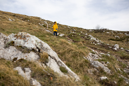 A young boy in a yellow windbreaker is hiking on rocky terrain