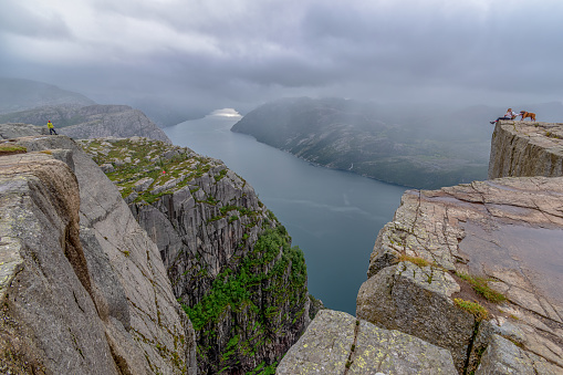 Preikestolen - Pulpit Rock,  Norway; July 12, 2020 - Young adults and a dog admiring the view from the Pulpit Rock over Lysefjorden.