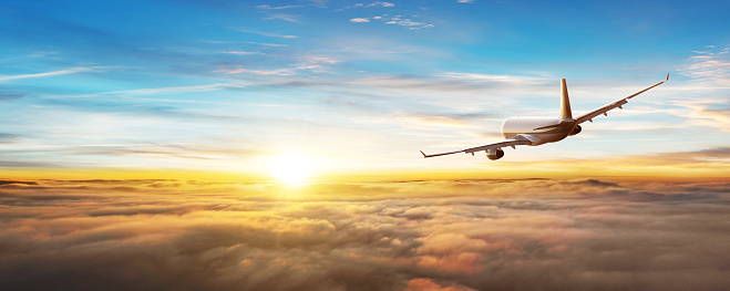 Commercial airplane flying above clouds, backside view. Sunset light