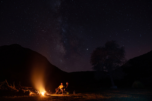 Friends sitting on camping chairs by bonfire under the stars in nature. Shot during night with a full frame mirrorless camera.