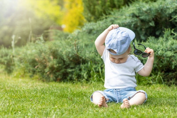 Little boy is taking off his hat holding sunglasses\