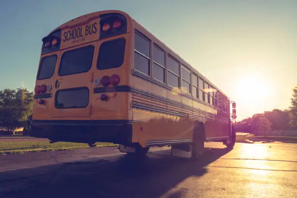 Photo of Low angle view of yellow school buss from right rear at dusk looking into setting sun