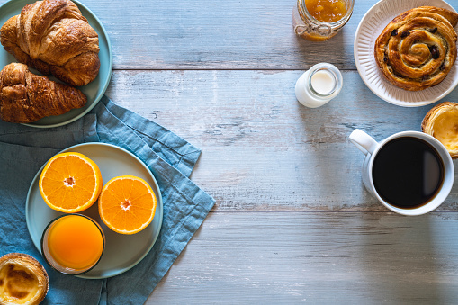 Breakfast Coffee with pastries Cinnamon roll croissant and Portuguese egg tart with orange juice on light blue table