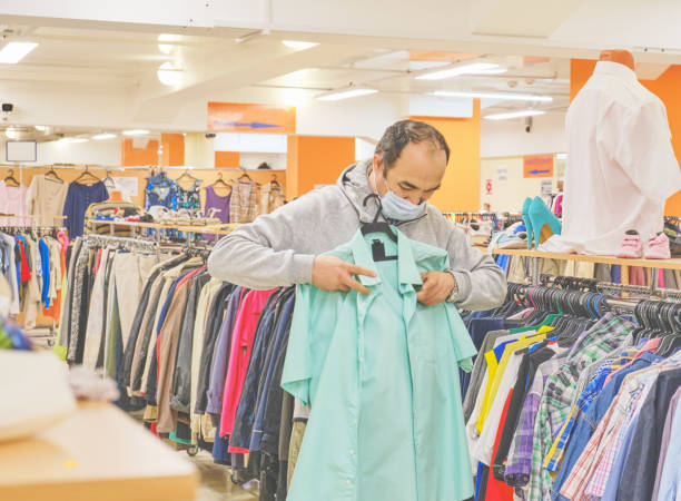 istock Mature man in mask choosing clothes at Second hand store. 1257068464
