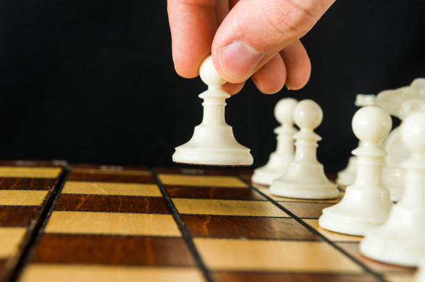 The part of a man's hand that makes the first move in a chess game, raising and moving a pawn one square forward. Dark background. stock photo