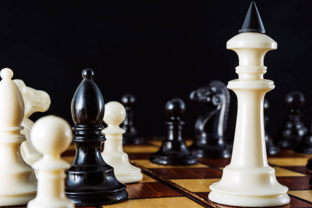 A white king on a chessboard surrounded by several pieces on a black background. stock photo