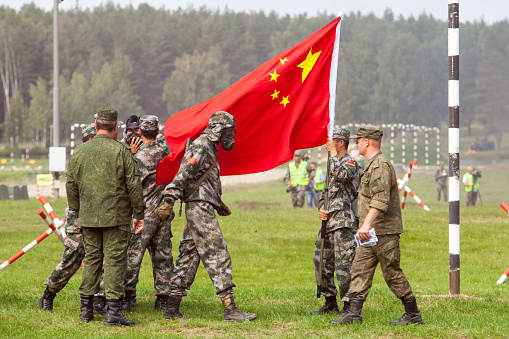 military competition ARMY 2018, Chinese army soldier in a chemical protection suit against the background of the flag of the people's army of China Кostroma Region the town of Pesochnoye June 2018