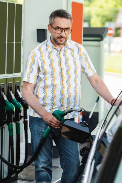 istock Selective focus of handsome man looking at camera while holding fueling nozzle near car on car refueling station 1257082565