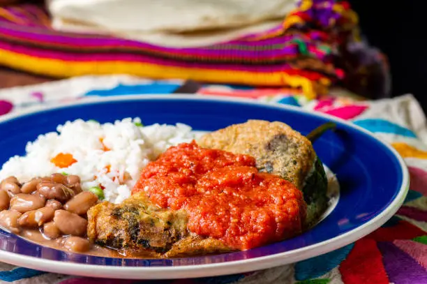 Mexican stuffed chilies (Chiles Rellenos), poblano chilis filled with cheese and coated with a light batter. Served with beans, rice and red tomato sauce