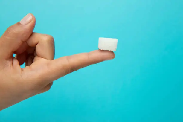 Sugar cube on the finger, blue background.