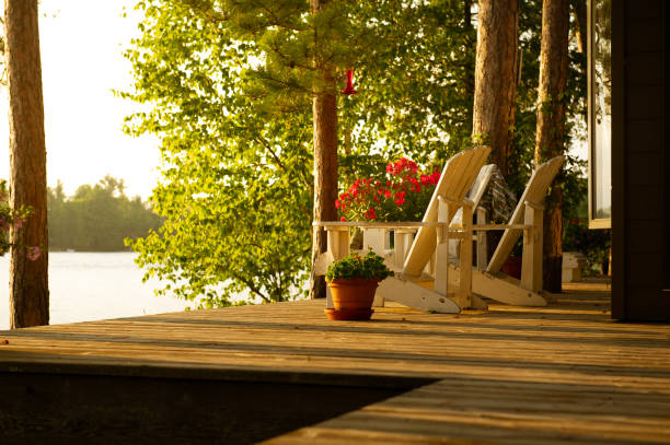 White Adirondack chairs sits on a cottage wooden deck at sunset stock photo