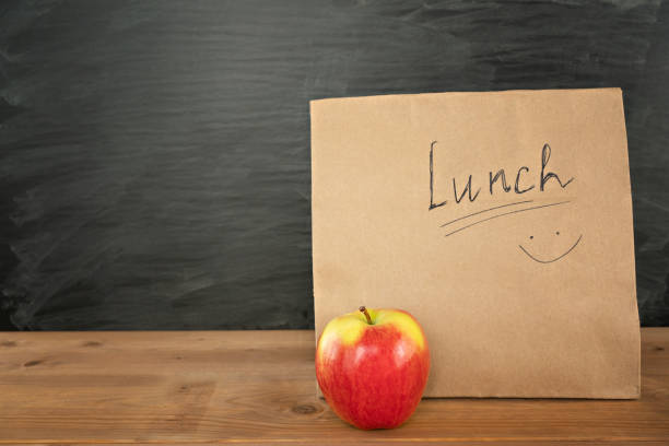 Eco friendly brown paper lunch bag on wooden table with red apple. Chalk board on background. Back to school concept Eco friendly brown paper lunch bag with smile on wooden table with red apple. Chalk board on background with copy space. Back to school concept.Time for snack at school. Education. Space for text. lunch break stock pictures, royalty-free photos & images