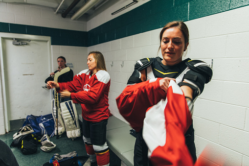 A female hockey player gets ready to put her equipment and uniform on before a recreation league hockey game. She is putting on her team uniform. Image taken in Utah, USA.