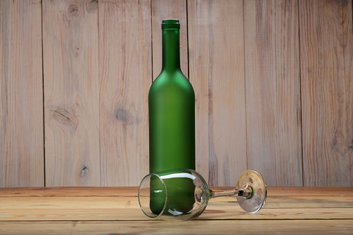 green empty wine bottle with goblet on wooden table and wooden planks background
