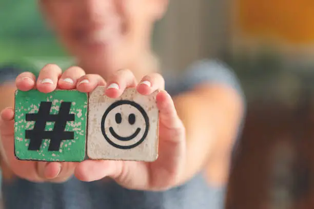 Woman holding a hashtag smiley emoticon sign and smiling. Online influencer liking happiness concept.