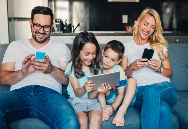 Relaxing at home with wireless technology. Portrait of a smiling young family with two kids using smart phones and digital tablet on the sofa at home. family dependency mother family with two children stock pictures, royalty-free photos & images