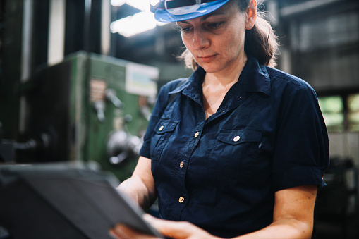 Image of a woman working in the heavy industry building as a quality control inspector, holding a digital tablet.