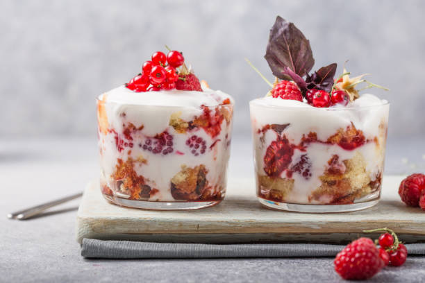 Layered trifle dessert with sponge cake, whipped cream and raspberries in serving glasses on light  background. With copy space Layered trifle dessert with sponge cake, whipped cream and raspberries in serving glasses on light  background. With copy space yogurt fruit biscotti berry fruit stock pictures, royalty-free photos & images