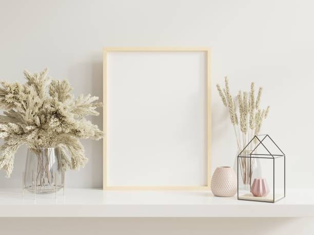 istock Wooden frame leaning on white shelf in bright interior with plants on the table with plants in pots on empty wall background. 1257115850