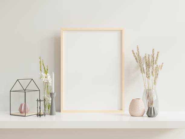 istock Wooden frame leaning on white shelf in bright interior with plants on the table with plants in pots on empty wall background. 1257115851