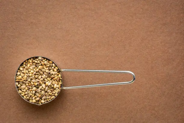 hemp seeds on metal measuring scoop, top view on brown handmade paper with a copy space