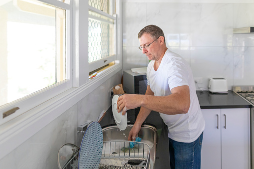 Mature Man Hand Washing Dishes at Home