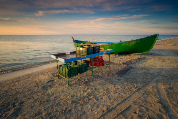Wooden table used by the fishermen to sort the fish before selling it when they arrive from fishing with crates on and under the table and a wooden boat on the Black Sea Coast in Romania at Corbu, Constanta County stock photo