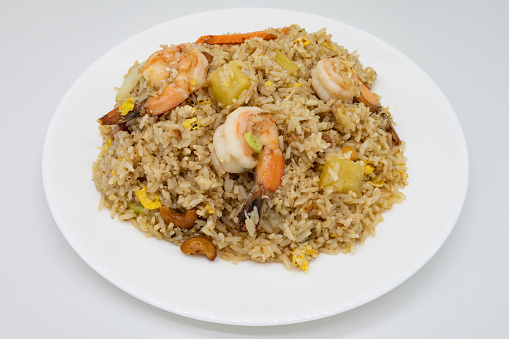 A large portion of Thai fried rice with shrimp and pineapple on a white plate with a white background