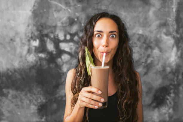 mujer feliz divertida bebiendo batido de leche de chocolate con cacao y riendo. concepto de bebida de verano. fondo de pared de hormigón gris. - mujer bebiendo leche fotografías e imágenes de stock