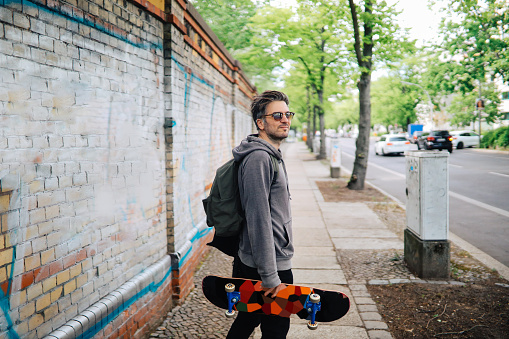 Skater man walking down the street and carrying his skateboard.