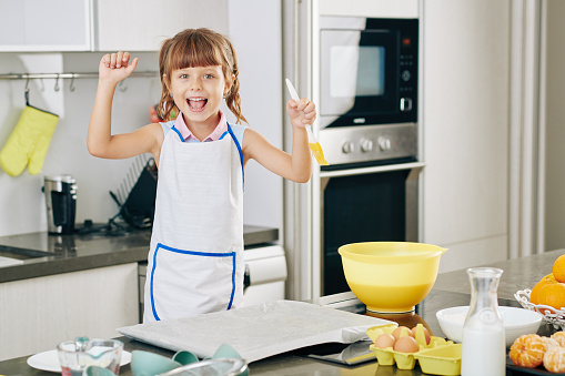 Portrait of happy excited little girl with silicone brush in hand enjoying baking cookies at home