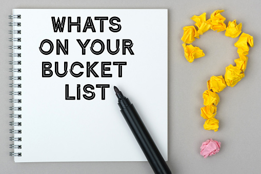 Hand with marker writing: Whats On Your Bucket List. Notepad and question mark.