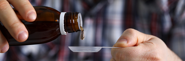 Letterbox view of sick man holding in hands vial with syrup close-up. Seasonal disease prevention and treatment or supplement and food additives with vitamins and omega 3 concept