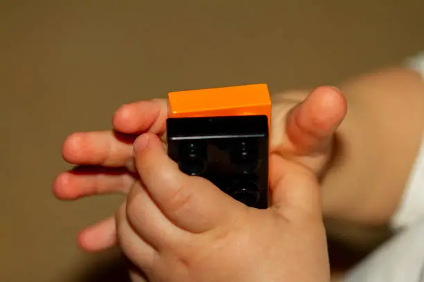 Close up image of an infant baby's hands as he or she is trying to interlock two toy bricks. Image is useful to demonstrate motor development, fine motor skills, balance, precision, baby growth themes